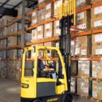 Photo of a man operating a Hyster E50XN in a warehouse, lifting a pallet out of a rack system.