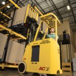 Photo of a man operating a Hyster stand-up 3-wheel electric forklift in a warehouse.