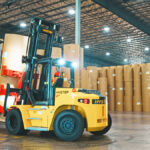 Photo of a high-capacity Hyster forklift equipped with a Bolzoni-Auramo jumbo paper roll clamp working inside a warehouse.