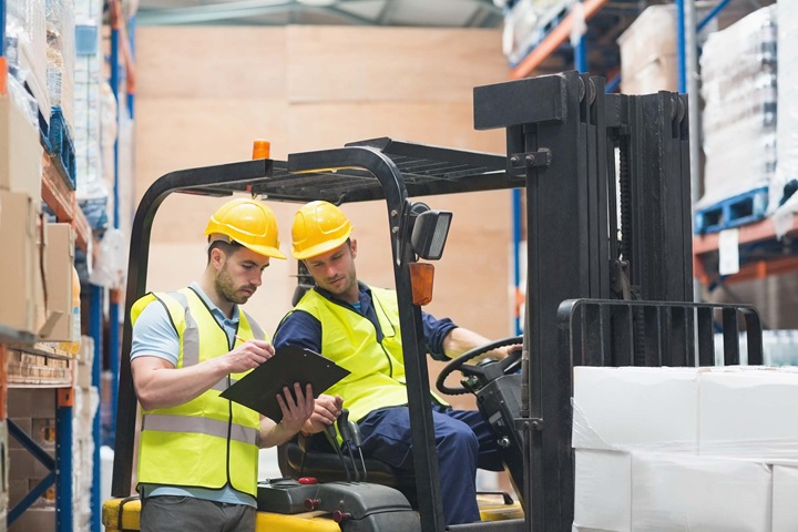 Forklift-Training-and-Certification Warehouse manager talking with seated forklift operator about safety training.