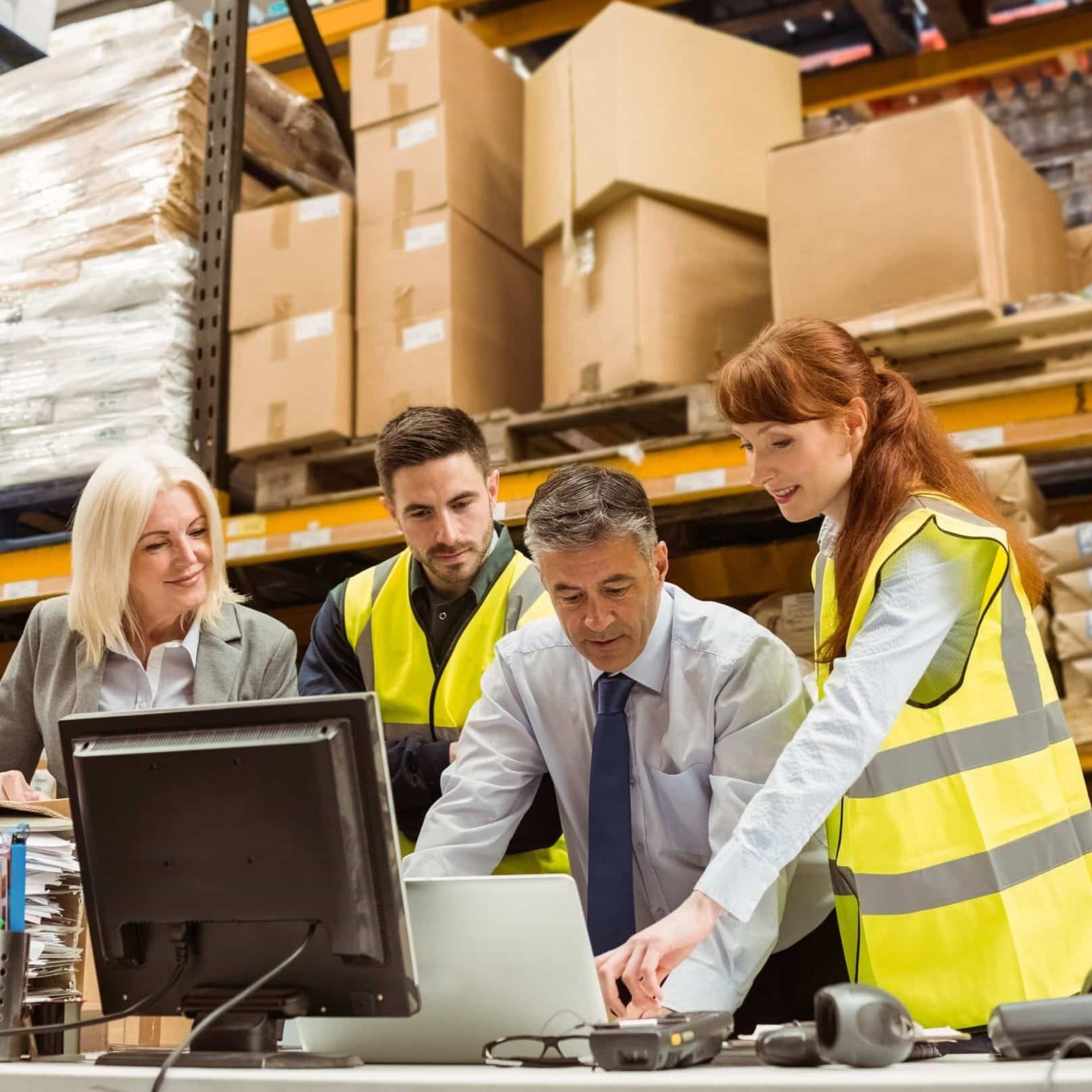 Four people reviewing plans on a desk inside a warehouse.